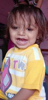 Smiling baby with brown hair, wearing a yellow shirt.