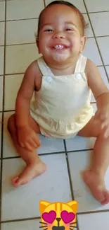 Smiling baby in beige outfit sits on a tiled floor.