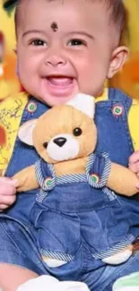 Happy baby in overalls with a teddy bear, smiling brightly.