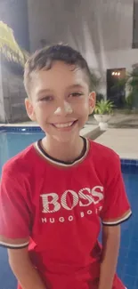 Smiling boy in red shirt by a pool, evening setting.