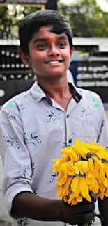 Young boy smiling, holding a bunch of yellow flowers.