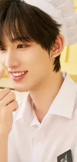 Smiling chef in white uniform against yellow kitchen background.