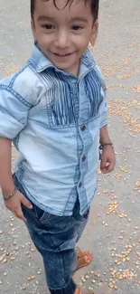 Smiling child in denim outfit standing outdoors.