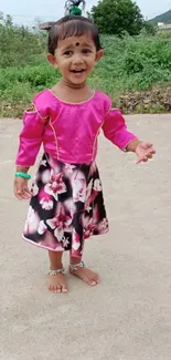 Smiling child in pink floral dress outdoors.