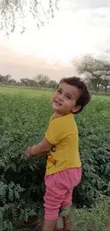 Smiling child in green field with trees and pastel sky.