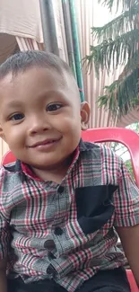 Smiling child in plaid shirt on red chair outdoors.