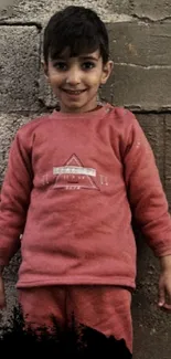 Smiling child in red clothing against a textured wall.