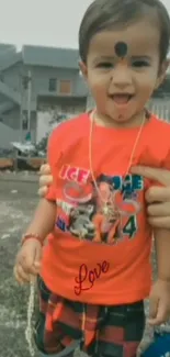 Adorable child in a vibrant red shirt smiling playfully outdoors.