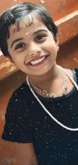 Smiling child with sparkling black dress and pearls.