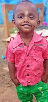 Smiling child in pink shirt standing outdoors with a happy expression.