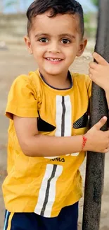 Boy in yellow shirt smiling outdoors against a blurred background.