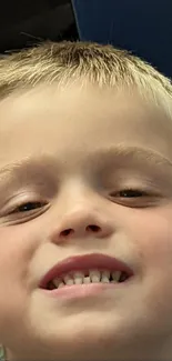 Mobile wallpaper of a smiling child with blonde hair against a blue and beige backdrop.