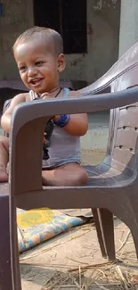 Smiling child sitting on a brown plastic chair outside.