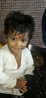 Adorable child with red mark, smiling joyfully in traditional attire.