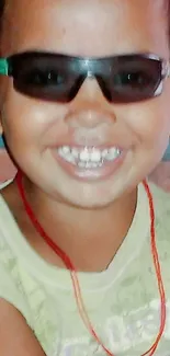 Child smiling with sunglasses and red necklace.