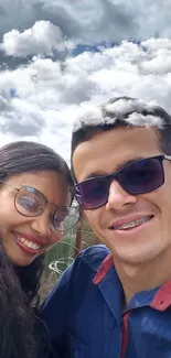 Smiling couple under a cloudy sky.