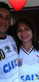 Couple in matching football jerseys under a red heart.