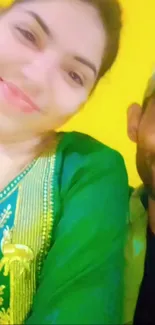 Couple smiling in traditional attire with a yellow background.