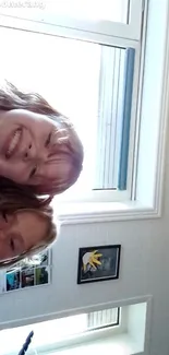 Two smiling kids leaning against a window.