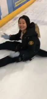 Smiling girl sitting on an ice rink with a joyful expression.