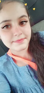 Young woman with heart emoji filter in a blue top, sitting in a car.