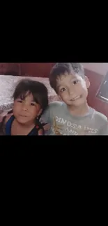 Two smiling children sitting together on a cozy bed.