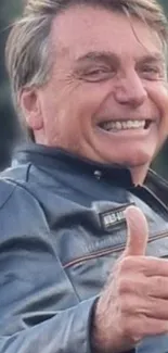 Man smiling in leather jacket with thumbs up in outdoor setting.