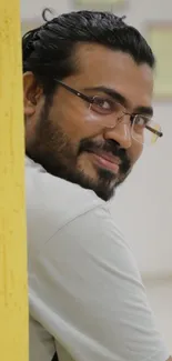 Portrait of a smiling man with glasses against a yellow background.