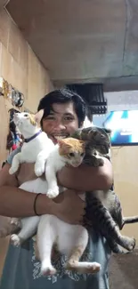 Man smiling while holding four cats indoors.