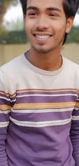 Smiling person wearing striped shirt in an outdoor setting.