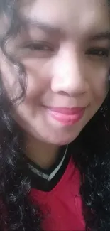 Close-up portrait of a smiling person with curly hair and pink shirt.