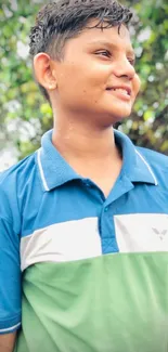 Smiling teen in blue and green shirt outdoors.