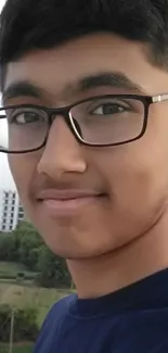 Portrait of a smiling teenage boy with glasses against a city background.