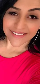 Woman smiling in bright pink shirt with natural makeup and hoop earrings.