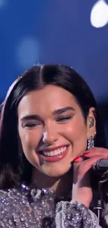 Woman singing on stage, wearing a sparkling dress, with a vibrant smile.