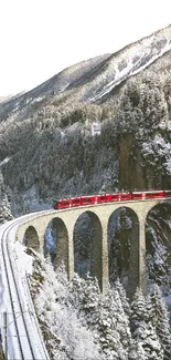 Red train on a snowy mountain viaduct, serene winter landscape.