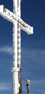 Snow-covered cross under clear blue sky on a mountain.