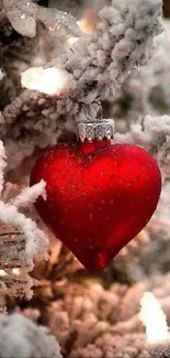 Red heart ornament on snowy Christmas tree.