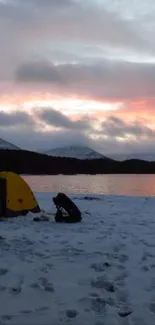 Snowy campsite by a lake during a vibrant sunset, with tents and a scenic view.