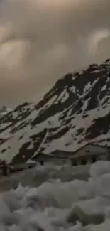 Snowy mountain landscape with cloudy sky and rustic buildings.