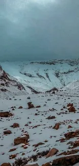 Snowy mountain landscape with rocky terrain under a teal blue sky.