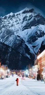 Snowy street leading to a majestic mountain at night with vibrant lights.