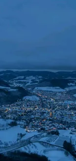 Aerial view of a snowy city at night with blue tones and glowing lights.