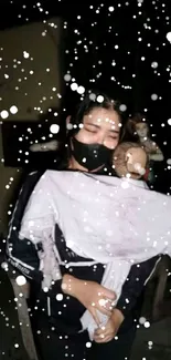 Person holding a child surrounded by snowflakes at night.