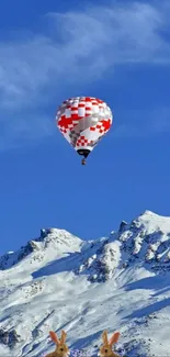 Hot air balloon over snowy mountains with blue sky.