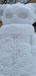 A snow sculpture of Yoda in a snowy backyard setting.