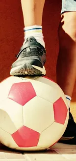 Shoe resting on a red and white soccer ball.