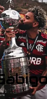 Soccer player kissing trophy on field.