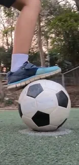 Foot balancing on soccer ball on turf field, showcasing athletic skill.