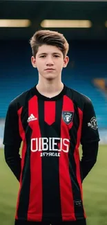 Young soccer player standing on field in a red and black uniform.